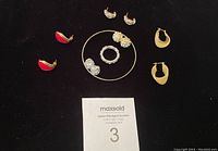 Full lot including various costume earrings, a ring, and a bangle arranged on black background with auction card