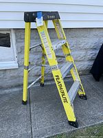 Side angle view showing yellow fiberglass frame, black top platform, four aluminum steps, metal braces, and black plastic feet.