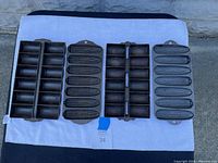 Four cast iron cornbread pans shown on white cloth background. The pans include two marked (Griswold and Warner Ware) and two unmarked.