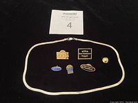 Full view of sterling silver herringbone necklace and six vintage pins arranged on black background with auction lot number