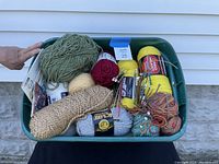 Large bin filled with assorted yarn skeins of various colors and weights along with knitting needles inserted into the yarn.