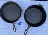 Two cast iron skillets side by side on white cloth, showing handles and overall shape