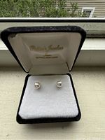 Pearl stud earrings on white cushion inside black velvet box with Patten's Jewelers branding visible on box lid, showing front-facing view of earrings.