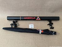 Closed umbrella with two mounting brackets and carrying case arranged flat on a surface