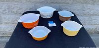Lot of five small Pyrex casserole bowls displayed on black cloth, various vintage patterns and colors.