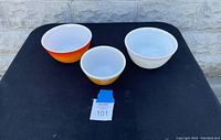 Front view of three vintage Pyrex mixing bowls: medium orange ombré, small yellow, medium white with red rim.