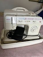 White Singer sewing machine with multiple stitch options, power cord, and foot pedal visible inside the carrying case on a patterned fabric surface.