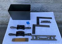 Lot of vintage Stanley tools displayed on white cloth, including a black metal storage box, machinist square, folding ruler, two wooden plane handles, and a Stanley Sweetheart level.