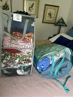Front view of the mesh carry bin filled with various folded fleece fabrics including floral, animal print, and solid colors, placed on a bed.