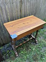 Full view of the vintage wooden table showing spindle legs, smooth tabletop with natural wood grain and knots, and front drawer.