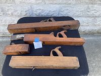 Six vintage wooden hand planers displayed on a black surface outdoors with stone wall background, showcasing varying sizes and handle styles.