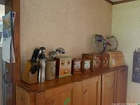 Wide shot showing the wooden bread box, four wooden canisters, tea and coffee box, utensil block with knives, water bottle, and a ceramic utensil holder with ladles and spoon on top of a wooden sideboard.