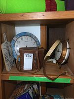 Clock on wooden board decorated with musical notes and instruments, round clock with blue rim, vintage metal electric clock, and leather binocular case on cubby shelf