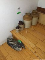 Photo showing all items grouped on wooden floor: two large mustard crocks, two smaller finger jugs, and fabric loon decoy