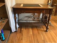 Solid wood vintage desk viewed from the front showing the single drawer with two metal handles and a lower shelf. Turned legs provide support.