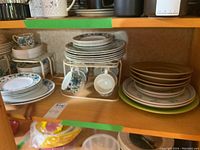 Photo showing stacked Midwinter Spanish Garden dinner plates, cups on stand, saucers, and additional plates in a mixed set.