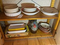 Top shelf with multiple round pie plates, pasta bowl, and white nesting dishes with woven baskets.