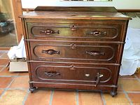 Front view of antique solid wood dresser showing three drawers with decorative carved pulls, top raised back edge, and bun feet.