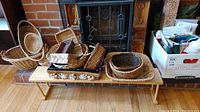 Photo showing assorted woven baskets on a wooden folding shelf in front of a fireplace, with gift wrap and bags in boxes nearby.
