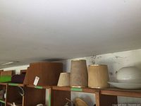Multiple fabric lamp shades in brown and beige color tones on top of wood cabinet.