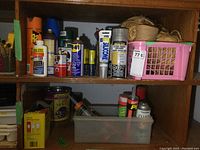 Two wooden cubbies containing various cans and bottles of lubricants, adhesives, pest control sprays, plus a pink plastic basket with twine.