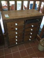 Front view of antique wooden cabinet showing multiple drawers with white knobs, one drawer missing.