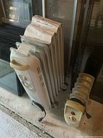 Photo shows two oil heaters: a larger white Honeywell heater with dual controls and a smaller beige heater with a rotary dial.
