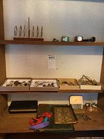 Overall lot showing boxes with pins, watches, tie clips, book covers, and memo holder on wooden shelves and table.
