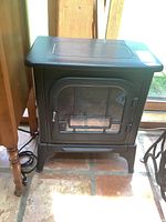 Full frontal view of metal portable heater designed as a faux fireplace with glass door and metal grid.