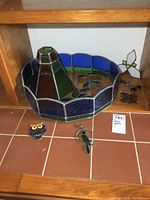 Round stained glass lamp shade with blue and green glass, stained glass sun catchers on tile surface beneath it