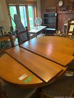 Round solid oak table shown expanded with two of four leaves inserted, showcasing the midsection join and wood grain.