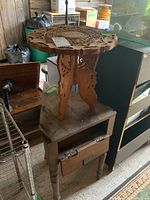 Side view of wooden side table with ornate carved top and three legs, hinged door visible