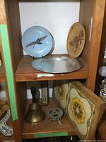 Overview of wooden cubbies containing plates, bell, metal tray, thermometer, trivet, and another decorative plate.