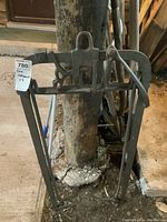 Metal hay fork with curved tines and sturdy frame, showing rust and wear, leaning against a wooden post in a garage setting.