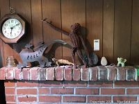 View of the animal theme items on a brick mantel, including the clock, metal lizard, rattan monkey, glass insulator, and several small animal figures.