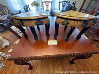 Pair of two Asian style corner stools or side tables with black and gold detailing on legs, placed side by side on wooden table.