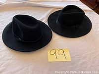 Two black wide brim hats on white surface with a numbered note