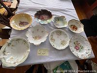 Top-down view of eight vintage porcelain bowls with varying floral patterns on white tablecloth showing condition and design details.