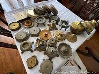 Group photo of 22 brass and metal candle holders and bases of different styles and sizes arranged on a white cloth-covered table.
