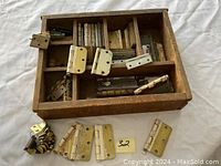 Box containing multiple brass hinges of various sizes and styles, some laid out in front