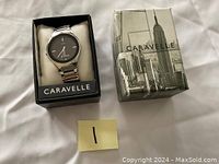 Front view of Caravelle wristwatch in original box, showing black dial and silver band.