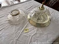 Two different styles of ceiling glass lamps side by side on a white cloth. One has a swirl-patterned glass shade with brass rim, the other a cut glass dome with brass mount.