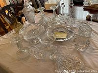 A collection of various crystal and glass items arranged on a cloth-covered table including candy dishes, candle holders, and decorative bowls with various cut glass patterns.
