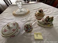 Photo showing a crystal candy dish with gold accent lid, porcelain egg with colorful flowers, floral porcelain box with gold trim, and a porcelain couple figurine on table.