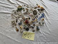 Overview of lot laid out on white cloth, showing variety of jewelry pieces including earrings, rings, pins, bracelets and necklaces.