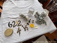Photo showing used metal door numbers and assorted small metal tools and parts on a white cloth-covered table.
