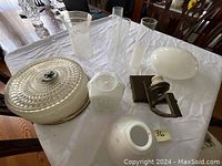 Five items on white cloth on table including 4 glass shades and one metal ceiling light fixture. Shades vary in shape and texture.