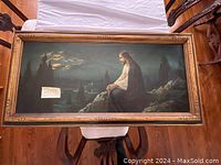 Photo of a large horizontal framed painting depicting Jesus praying outdoors at night with a misty mountainous background and moonlit sky. The frame has an ornate gold finish and visible small scratch.