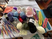 View of assorted yarn skeins, knitting needles, crochet hooks, and plastic yarn looms on a table.