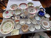 Top-down photo of a collection of vintage porcelain plates, bowls, cups, and trays, showing various floral patterns and decorative motifs.
